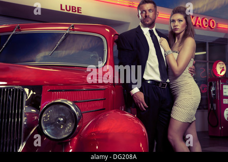 Gut gekleideter Mann und Frau neben roten Oldtimer vor Tankstelle Stockfoto