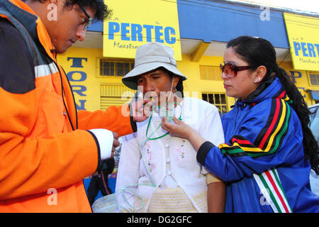 El Alto, Bolivien. 12. Oktober 2013.  Ein Konkurrent erhält ein süßes (um den Blutzuckerspiegel zu erhöhen) und Sauerstoff zu helfen, von den Auswirkungen der Belastung in großer Höhe nach Abschluss einer Cholitas Radrennen für indigene Aymara Frauen erholen. Das Rennen findet auf einer Höhe von etwas mehr als 4.000 m entlang der Hauptstraßen in der Stadt El Alto (oberhalb der Hauptstadt La Paz) für bolivianische Womens Tag wurde gestern Freitag, den 11. Oktober statt. Bildnachweis: James Brunker / Alamy Live News Stockfoto