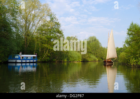 Yacht segeln bis River Bure, Norfolk Broads, England, vorbei an Urlaub Start Hausboot festgemacht unter Bäumen. Stockfoto