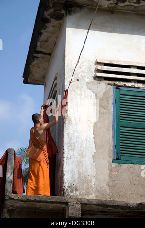 Ein buddhistischer Mönch hängt eine orange Safranrobe auf einer Wäscheleine an einem buddhistischen Tempel in Phnom Penh, Kambodscha. Stockfoto