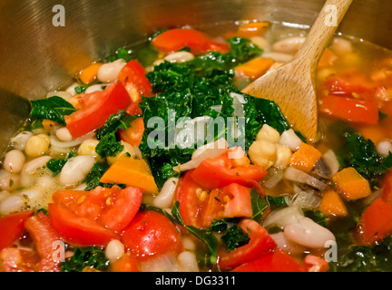 Das Rühren der Topf der vegane Gemüsesuppe mit frischen Grünkohl Tomaten Kichererbsen Karotten und Zwiebeln. Eine sehr gesunde und kräftige Suppe. Stockfoto