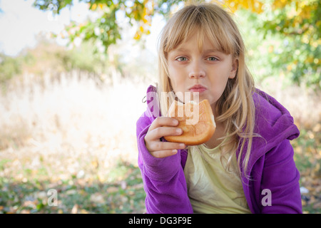 Kleines blondes Mädchen im Herbst Park frisst kleine Kuchen Stockfoto