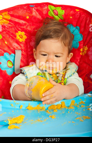 Chaotisch Babyjungen Püree selbst Essen und sitzen auf Stuhl Stockfoto