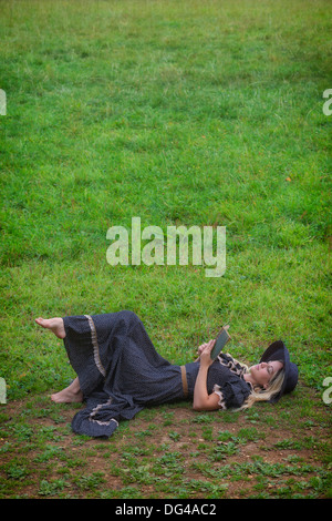 eine Frau in einem romantischen Kleid ist auf einer Wiese liegend ein Buch lesen Stockfoto