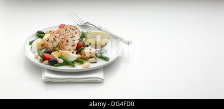Niscoise-Lachssalat auf einem weißen Teller mit Dressing in einer Schüssel Stockfoto
