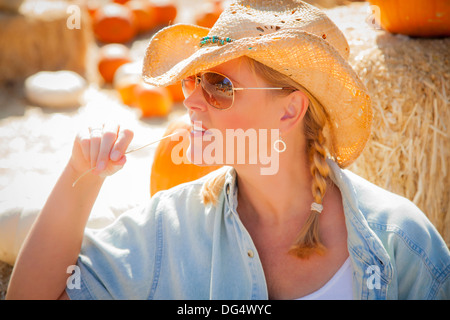 Schöne blonde weibliche Rancher einen Cowboy Hut in einem Kürbisfeld kauen auf ein Stück Stroh. Stockfoto