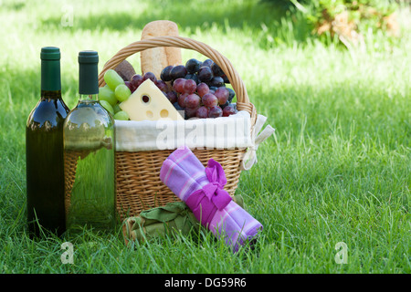 Outdoor-Picknick-Korb mit Brot, Käse und Trauben und Wein-Flaschen auf Rasen Stockfoto