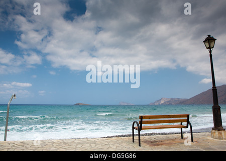 Eine Bank, eine Laterne und einer öffentlichen Dusche an einem leeren Strand auf Kreta. Das Wetter wird bald zum schlechten Witz schwere Wolken am Himmel Stockfoto