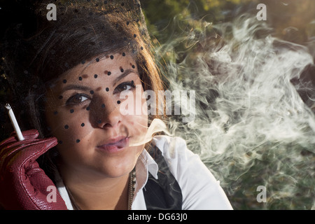 Geheimnisvolle schöne Brünette raucht eine Zigarette bei Gegenlicht. Stockfoto