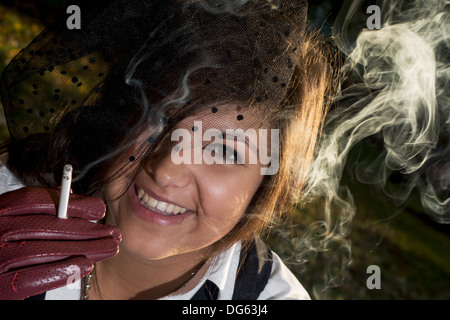 Lächelnde junge Frau raucht eine Zigarette bei Gegenlicht. Stockfoto