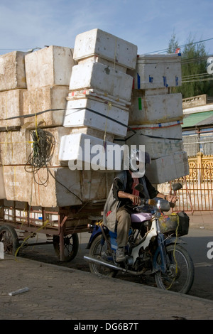 Eine Lieferung Mann auf einem Motorrad wird auf seinem Weg mit einer großen Belastung von Boxen auf einer Straße in Phnom Penh, Kambodscha gestoppt. Stockfoto