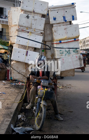 Eine Lieferung Mann auf einem Motorrad wird auf seinem Weg mit einer großen Belastung von Boxen auf einer Straße in Phnom Penh, Kambodscha gestoppt. Stockfoto