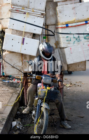 Eine Lieferung Mann auf einem Motorrad wird auf seinem Weg mit einer großen Belastung von Boxen auf einer Straße in Phnom Penh, Kambodscha gestoppt. Stockfoto