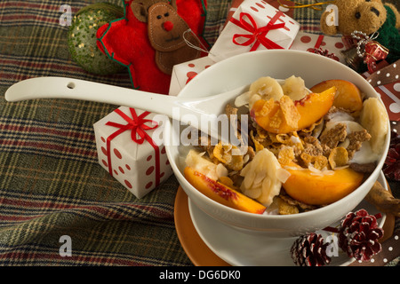 Schüssel mit Müsli, Obst und Joghurt, Plaid, Geschenke und Weihnachtsschmuck Stockfoto