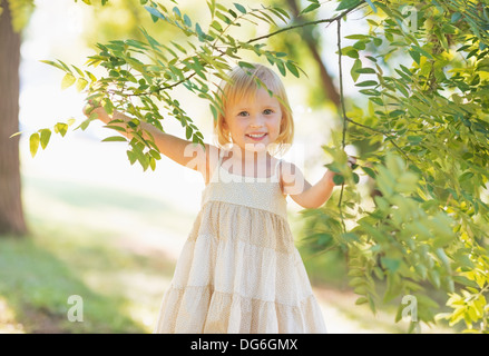Porträt von lächelndes Babymädchen mit Blick vom Baum Laub Stockfoto
