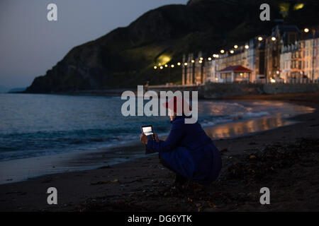 Aberystwyth Wales UK, 15. Oktober 2013 Frau mit ihrem Tablet-Computer, um den dramatischen Himmel in der Dämmerung über die Cardigan Bay am Strand bei Aberystwyth Wales UK zu fotografieren.  Nach einem warmen trocken und sehr sonnig Tag im Westen von Wales, ist die Prognose für die nächsten paar Due zur Steigerung der Wolke und Duschen der Regen Photo Credit: Keith Morris/Alamy Live-Nachrichten Stockfoto