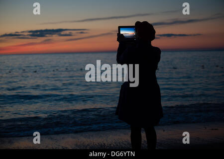 Aberystwyth Wales UK, 15. Oktober 2013 Frau mit ihrem Tablet-Computer, um den dramatischen Himmel in der Dämmerung über die Cardigan Bay am Strand bei Aberystwyth Wales UK zu fotografieren.  Nach einem warmen trocken und sehr sonnig Tag im Westen von Wales, ist die Prognose für die nächsten paar Due zur Steigerung der Wolke und Duschen der Regen Photo Credit: Keith Morris/Alamy Live-Nachrichten Stockfoto