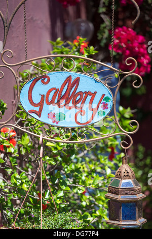 Blaues Schild die Wort-Galerie in rot und ist umgeben von einem grünen Garten in Santorin anzeigen Stockfoto