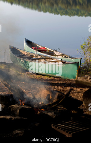 Zwei Kanus vertäut am Ufer eines Lagers mit einem Lagerfeuer beleuchtet im Vordergrund Stockfoto