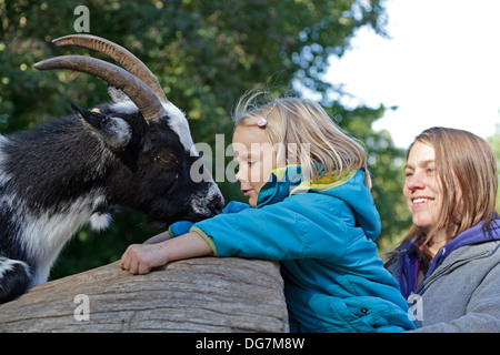 kleines Mädchen, eine Ziege, ihre Mutter hielt sie füttern Stockfoto