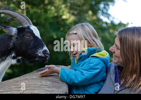 kleines Mädchen, eine Ziege, ihre Mutter hielt sie füttern Stockfoto