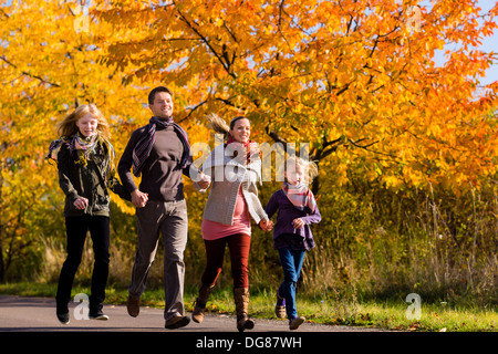 Junge Familie mit Mutter, Vater und Töchter zu Fuß durch bunte Bäume im Herbst oder im Herbst Stockfoto