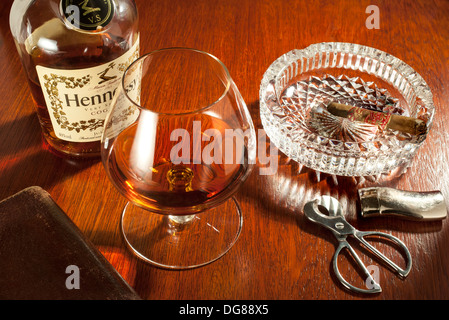 Schnaps und Zigarren - ein Cognac-Schwenker Glas Hennessy Cognac mit einem Teil rauchte Zigarre im Aschenbecher Stockfoto