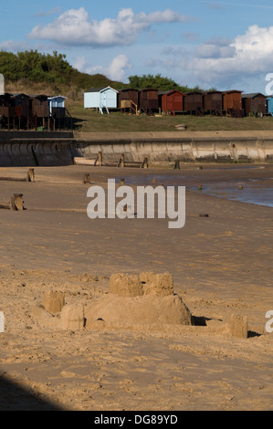 Die Sonne scheint auf eine Sandburg am Strand Frinton abgeschlossen. Strandhütten stehen im Hintergrund Stockfoto