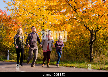 Junge Familie mit Mutter, Vater und Töchter zu Fuß durch bunte Bäume im Herbst oder im Herbst Stockfoto