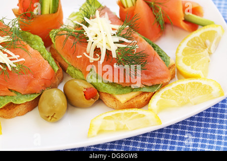 Sandwiches mit Lachs, Käse, Salat, Kräuter auf Teller, Oliven und Zitronen. Stockfoto