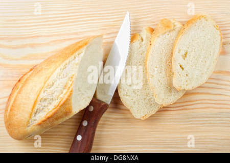 Frisch gebackenes Baguette in Scheiben geschnitten auf Holzbrett, Messer, Ansicht von oben Stockfoto