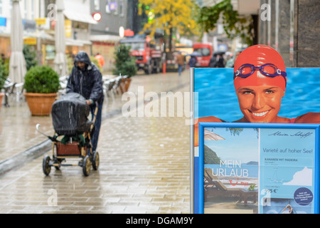 Werbeplakat zeigt hübsche Frau mit Kappe und Schwimmen Brillen und Vater mit Baby Buggy walking Zentrum im Regen Stockfoto