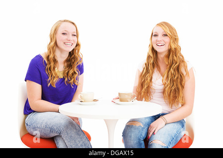 zwei Rothaarige Frauen sitzen am Tisch auf weißem Hintergrund lachen Stockfoto