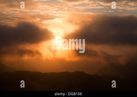 Wolken verdecken teilweise eine untergehenden Sonne über Seenplatte Berge Stockfoto