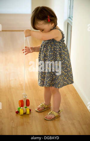 Babymädchen spielen mit einem hölzernen Spielzeug an einer Schnur Stockfoto