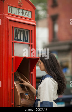 Mitte Erwachsene Frauen mit Geldautomat in einer öffentlichen Telefonzelle Stockfoto