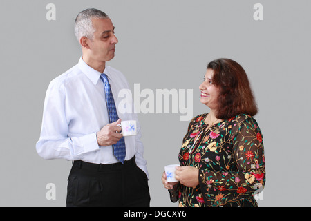 Groß, fair, mittleren Alter Mann, corporate look, Hemd und Krawatte, mit einer Tasse Kaffee mit einer kurzen mittleren gealterten lächelnde Frau Stockfoto