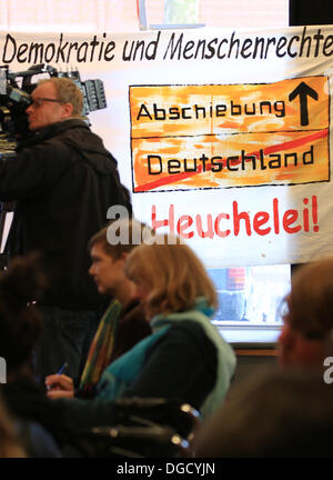 Hamburg, Deutschland. 18. Oktober 2013. Journalisten und Gäste sitzen vor einer Protest-Banner Darstellung ein Ortsname Schild mit der Aufschrift Deportation auf einer Pressekonferenz des Arbeitskreises Flüchtlinge "Lampedusa in Hamburg" in Hamburg, Deutschland, 18. Oktober 2013. Ein Flüchtling der Lampedusa-Gruppe hat eine Klage gegen Polizeiaktionen. Foto: CHRISTIAN CHARISIUS/Dpa/Alamy Live News Stockfoto