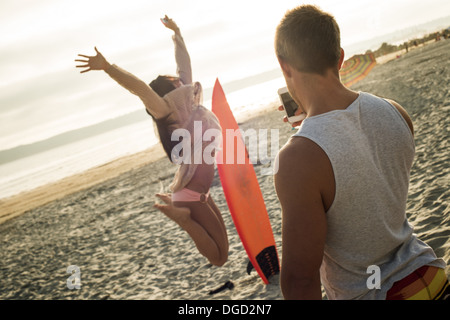 Junger Mann fotografiert Frau springen am Strand Stockfoto