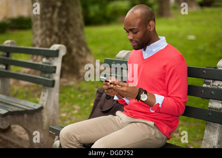 Junger Mann sitzt auf der Parkbank mit Handy Stockfoto