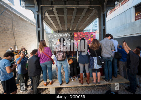 New York, USA. 18. Oktober 2013. Streetart-Fans strömen in West Chelsea Galerie Szeneviertel in New York die 18. Ausgabe von Banksy-Graffiti-Kunst, eine Zusammenarbeit mit den brasilianischen Künstlern, Os Gemeos sehen. Dieser Titel ist wie einer Museumsausstellung in eine Baulücke unter der High Line Park komplett mit "Museumswärter" Gruppenkontrolle behandeln eingerichtet. Die schwer fassbare Streetart-Künstler schafft Werke rund um die Stadt jeden Tag im Laufe des Monats Oktober. Bildnachweis: Richard Levine/Alamy Live-Nachrichten Stockfoto