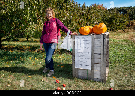 Eine Frau lehnt sich gegen Holz Kiste mit Kürbisse auf Papier und Zeichen lesen' auf die Pumpkin Patch - durch das Tor in das Feld Stockfoto