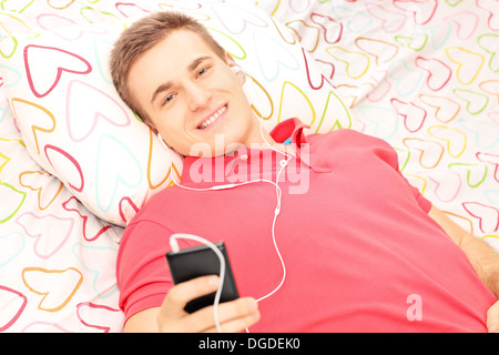 Lächelnd Jüngling auf einem Bett liegend und Musik vom Handy hören Stockfoto