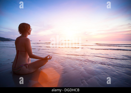 Junge Frau praktizieren Yoga am Strand bei Sonnenuntergang. Stockfoto