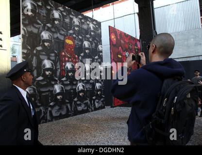 New York, USA. 18. Oktober 2013. Graffiti-Künstler Banksy, bekannt für seinen Stil Schablone arbeitet mit brasilianischen eineiige Zwillinge Os Gemeos, bekannt für ihr gelb gefärbten Cartoon Volk für "Besser aus als In" street Art passiert überall in NYC. Die Gemälde sind hing an einer Railroad Trestle in West Chelsea und bewacht um Verunstaltung zu verhindern. Bildnachweis: Nancy Kaszerman/ZUMAPRESS.com/Alamy Live-Nachrichten Stockfoto