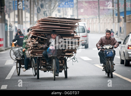 Mann mit Haufen von alten Abfall Brettern und Bohlen auf Dreirad-Zyklus mit auf Straße in Shanghai, China Warenkorb Stockfoto