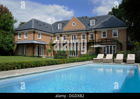 der Garten hinter dem Haus von einem großen Einfamilienhaus und Swimmingpool mit Liegestühlen Stockfoto