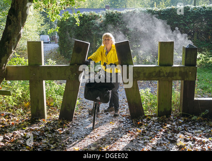 Eine Radfahrerin schiebt ihr Fahrrad durch eine Barriere auf der Route C2C im frühen Morgennebel, Washington, Nordostengland, Großbritannien Stockfoto