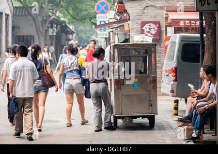 Chinesische Frau fängt eine kleine Fahrrad-Taxi an der Hauptstraße in der Jing Yang Hutong in Peking. Stockfoto