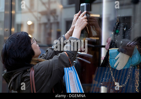 Junge Frau Tourist Fotos Mode speichern Anzeige in der New Bond Street, London mit smartphone Stockfoto